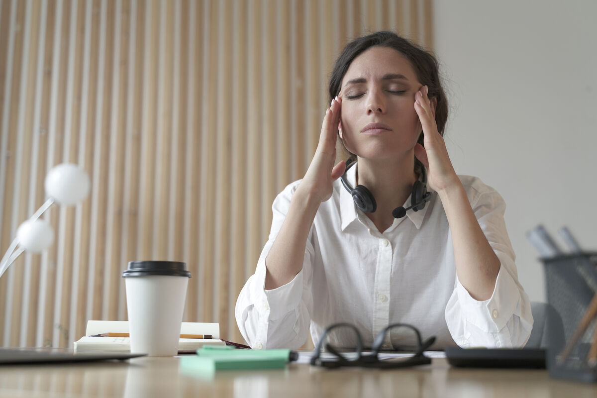 A woman at her desk, eyes closed, fingertips at her temples in a quiet moment of pause